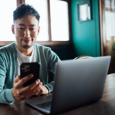 Man checking his cell phone in front of his laptop